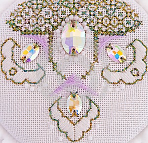 A handmade embroidery with white, purple and gold - green threads, white beads and crystals on it. 9. Close-up