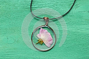 Handmade epoxy resin jewelry. pendant, rose in copper frame. dried flowers. herbarium, oshibana, phytotherapy. on green wooden