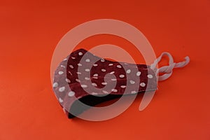 A handmade face mask made of circular patterned cloth placed on an orange background, washable and reusable