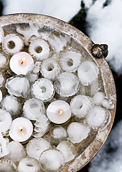 Handmade garden ice decoration in shape of mini bundt, Christmas trees, snowman with burning tea lights candles.