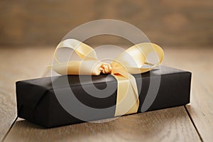 Handmade gift black paper box with yellow ribbon bow on wood table