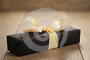 Handmade gift black paper box with yellow ribbon bow on wood table