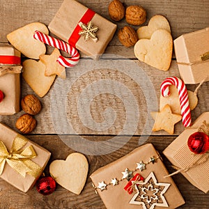 Handmade gift boxes, candy canes, walnut and gingerbread cookies on rustic wooden background, top view, copy space, frame.