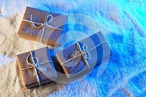 Handmade gift boxes from craft paper over snowy wooden table in blue light.