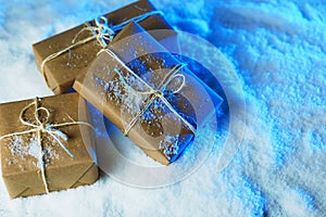 Handmade gift boxes from craft paper over snowy wooden table in blue light.