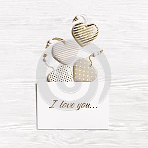 Handmade hearts from cotton cloth with golden color striped or dots and white empty paper for love message on white wood