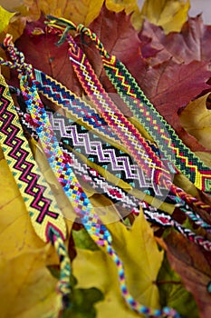 Handmade homemade colorful natural woven bracelets of friendship isolated on autumnal leaves background, beautiful bright colors