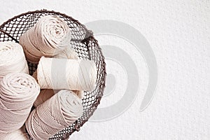 Handmade macrame braiding and cotton threads in basket on white background. Cotton macrame cords and ropes in wire basket. Good