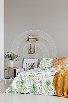 Handmade macrame and copy space on the empty grey wall of elegant bedroom with floral bedding on king size bed