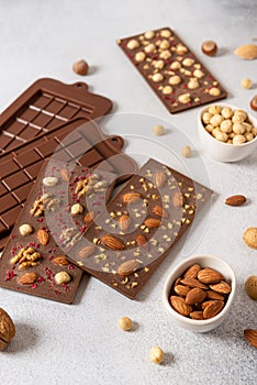 Handmade milk chocolate bars with nuts and dried fruits with molds and ingredients on white background. Side view