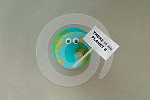 handmade model of planet earth with googly eyes holds a sign that says there is no planet b