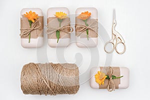 Handmade natural soap set decorated with craft paper, orange calendula flowers, skein of twine and scissors on white background .