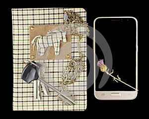 A handmade notebook on which lies a bunch of keys and a pendant in the form of an owl, and next to the smartphone on which lies