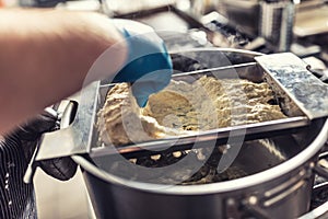 Handmade production of halusky from dough through sieve into boiling hot water