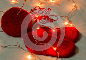 Handmade red color woolen christmas socks, chrochet needle and wool ball illuminated with miniature christmas lights. copy space