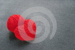 Handmade red yarn ball with heart made of red wool yarn on a gray woolen fabric background. Red warm heart like a symbol of love.