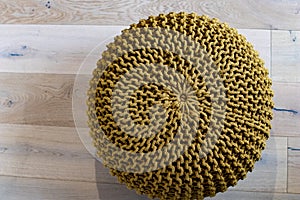 Handmade round circular soft mesh pouffe, handcrafted on a wooden parquet. Mustard-colored puff in apartment, woven with cotton
