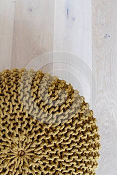 Handmade round circular soft mesh pouffe, handcrafted on a wooden parquet. Mustard-colored puff in apartment, woven with cotton