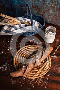 Handmade rye bread over a wooden table with spikes and cloth in a basket and a flour jar