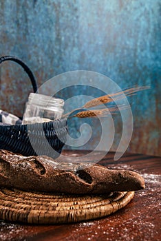 Handmade rye bread over a wooden table with spikes and cloth in a basket and a flour jar