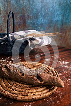 Handmade rye bread over a wooden table with spikes and cloth in a basket and a flour jar