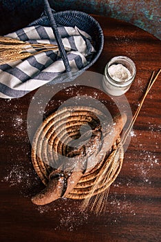 Handmade rye bread over a wooden table with spikes and cloth in a basket and a flour jar. Top view