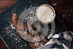 Handmade rye bread wrapped with a cloth over a stone table and a flour jar next to it