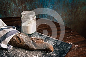 Handmade rye bread wrapped with a cloth over a stone table and a flour jar next to it