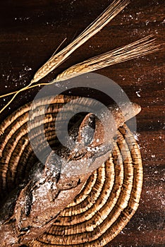 Handmade rye bread wrapped over a wooden table with spikes. Some flour has fallen on the table