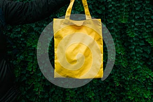 Handmade shopping bag on green plant background. Blank canvas bag, design mockup with hand