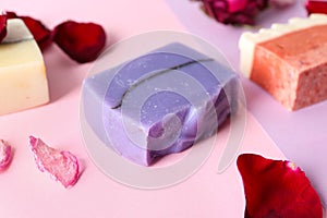 Handmade soap bars and flower petals on color background