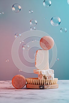 Handmade soap bars on natural bristle brush surrounded by bubbles on pastel pink and blue background.