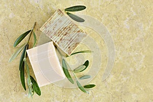 Handmade soap bars and olive branches on color background