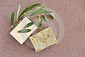 Handmade soap bars and olive branches on fabric background.
