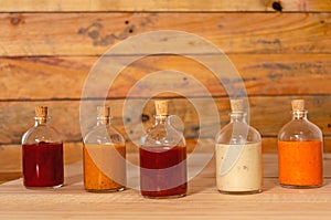 Handmade spicy sauces in glass bottles with cork on a colored wooden base - Salsas picantes hechas artesanalmente en botellas de photo