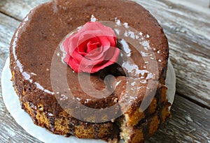 Handmade sponge cake with chocolate frosting. Small cake with cacao ganache glaze. Red sugar rose decorated. Homt pastry. Sweet photo