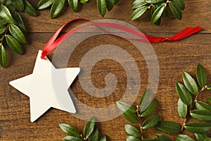 Handmade, star-shaped blank Christmas gift tag with red ribbon and natural evergreen decorations on rustic wood background