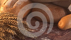 Handmade tasty bread lying on burlap on the wooden table with flour, wheat and ears of wheat