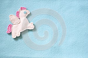 Handmade toy Pegasus on a baby blue felt background. Handmade blue flat lay. Sewing funny felt pony with wings.