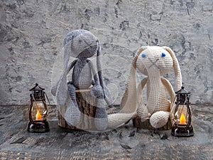 Handmade toys, amigurumi, crocheted bunnies sitting on stumps and lit lanterns