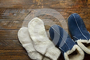 Handmade warm house shoes from sheepskin and sheep fur knitted woolen socks on wood background. Winter autumn eco fashion