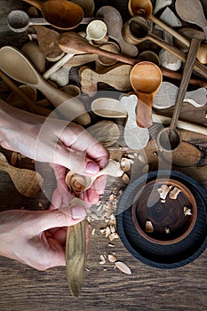 Handmade wooden utensils, top view female hands carve a wooden spoon with stock-knife, selective focus