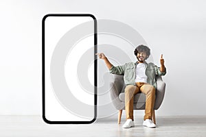 Handome young indian man pointing at huge smartphone, mockup