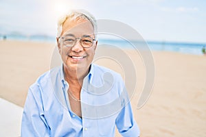 Handosme hispanic man with grey hair smiling happy at the beach, enjoying holidays on summer