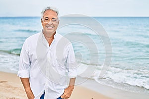 Handosme hispanic man with grey hair smiling happy at the beach, enjoying holidays on summer