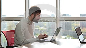 Handosome bearded man pondering while working on laptop.