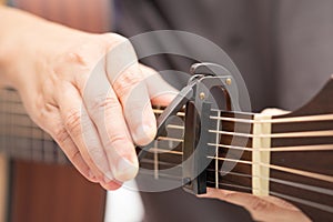 The hands are adjusting the capo to adjust the sound of the guitar.