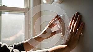 Hands adjusting a white light switch on a wall.