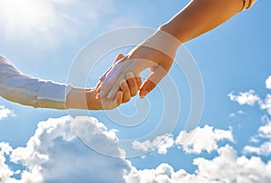 Hands of adult and child on blue sky background