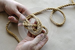 Hands of an adult man knit knots from hemp rope